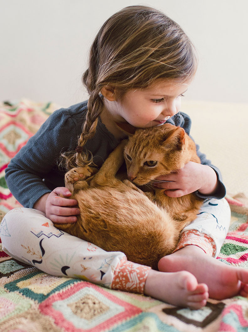 A young girl snuggles with her orange-haired cat.